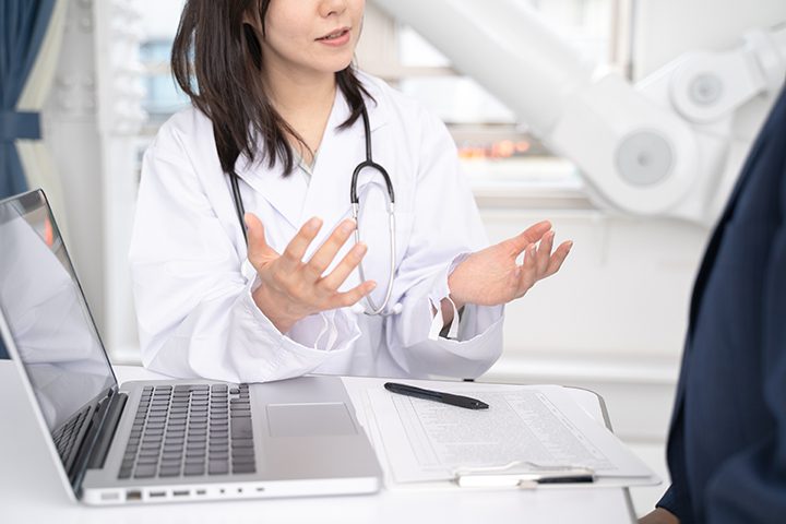 ノートパソコンを見ながら病状を説明する女医と男性患者の手元