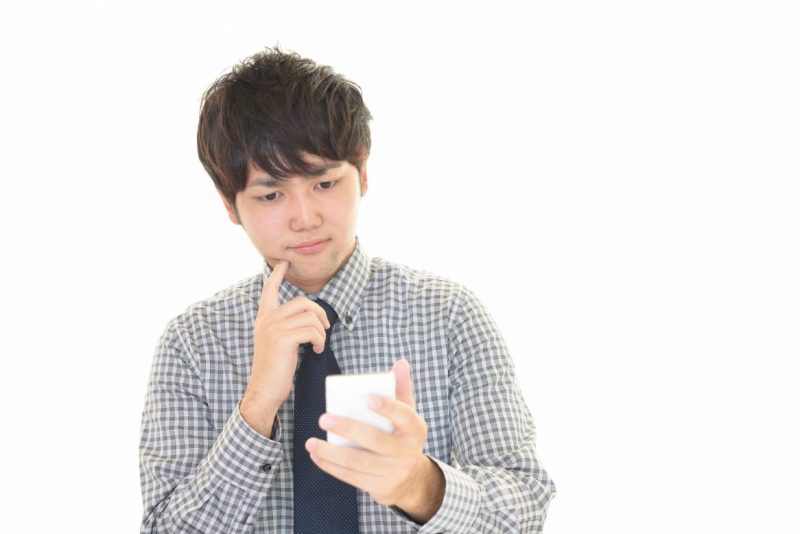 スマホを見ながら悩む男性