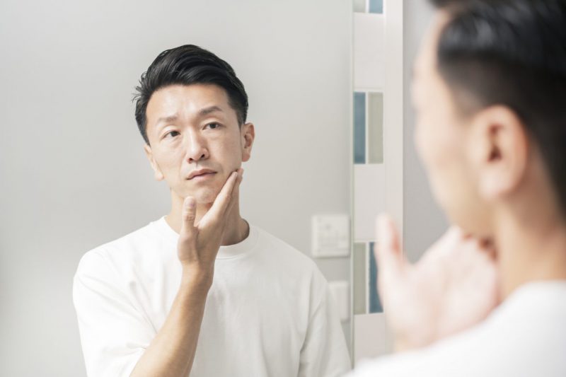 鏡を見て、肌の状態を確かめる男性