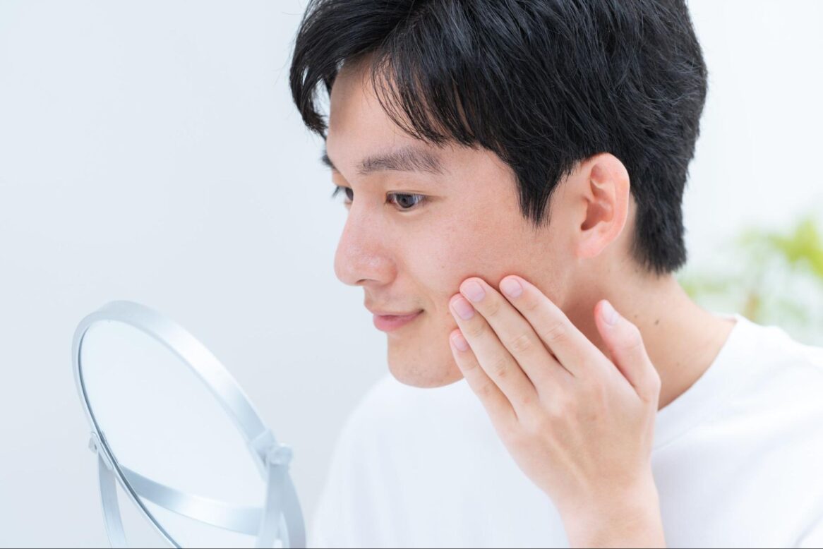 鏡を見て頬を触っている男性