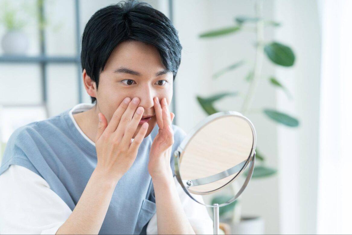 鏡を見て鼻あたりに触れている男性