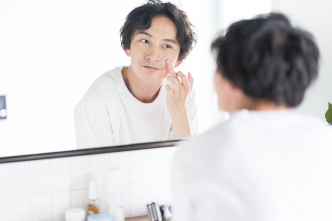 鏡を見て頬を触っている男性