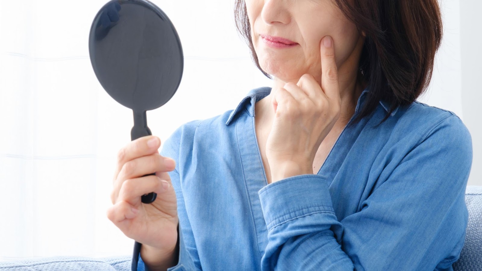 鏡を見ながらたるみを気にしている女性