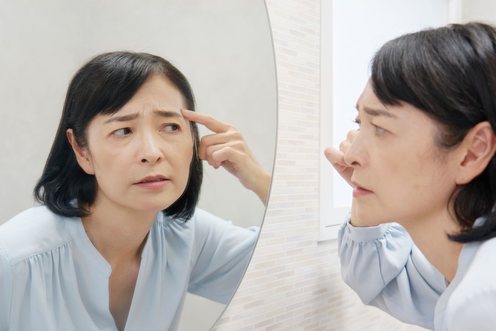 鏡を見ておでこのしわを気にする女性