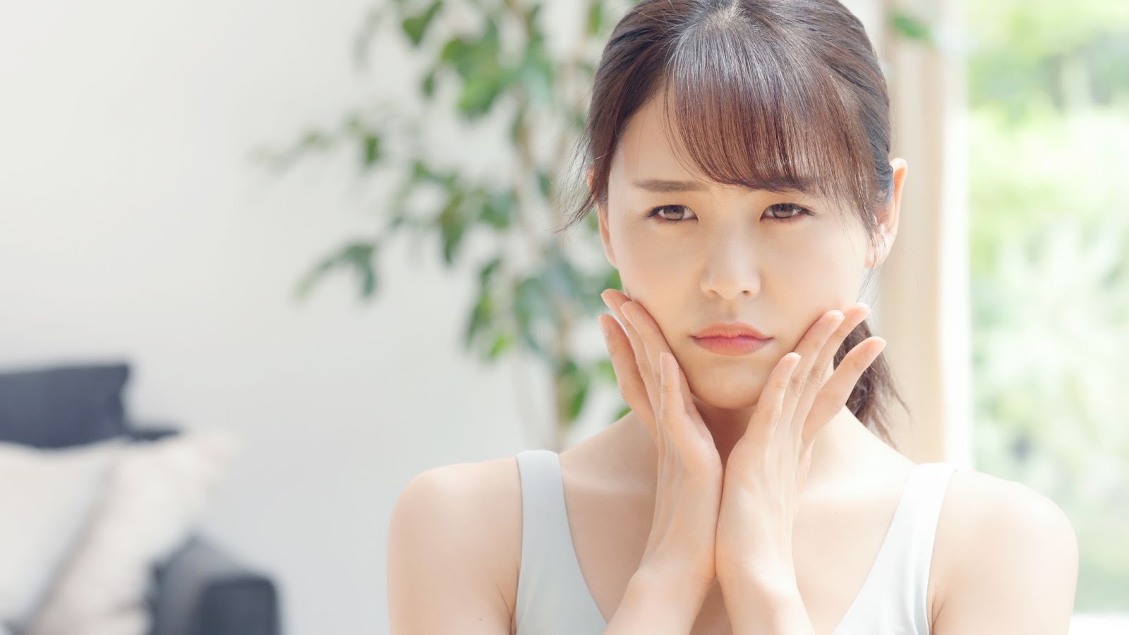 顔のたるみを気にして頬に手を当てている女性