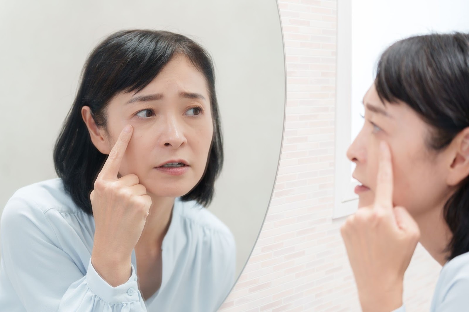 鏡を見て目の下のたるみを気にしている女性