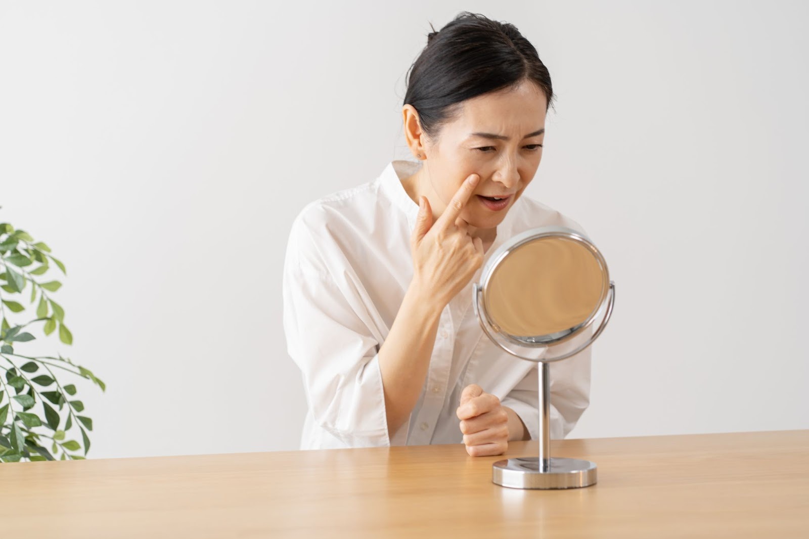 鏡を見て目の下のたるみを気にしている女性