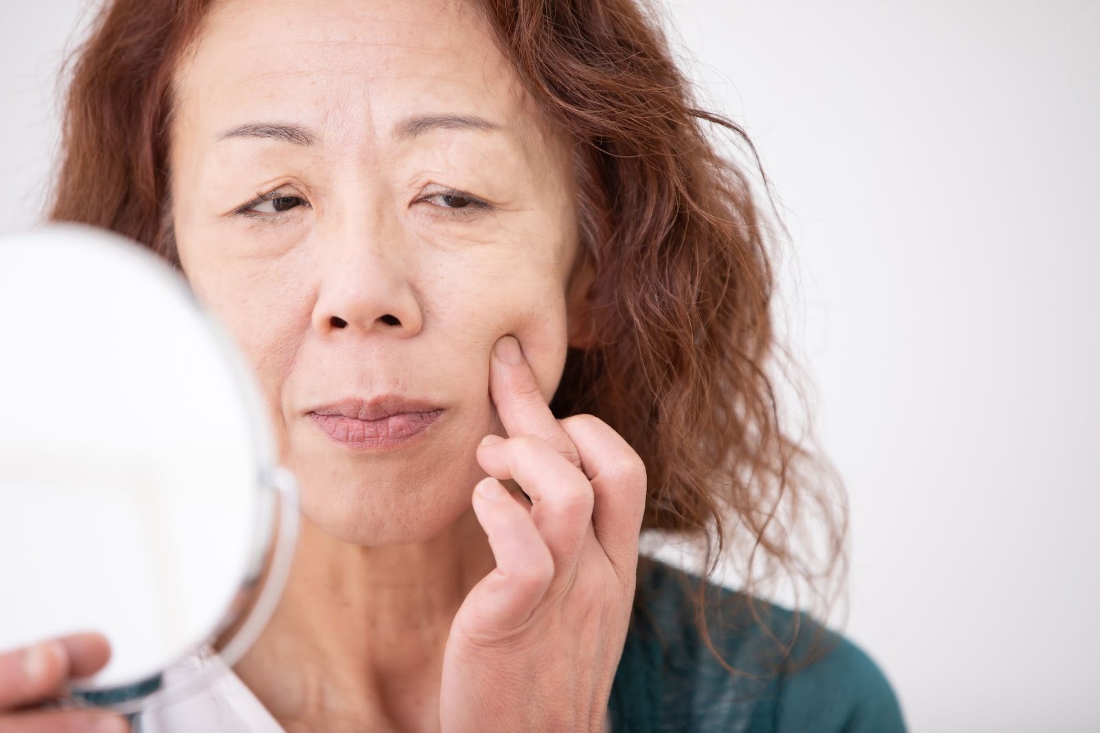 鏡を見て目の下のたるみを気にしている女性