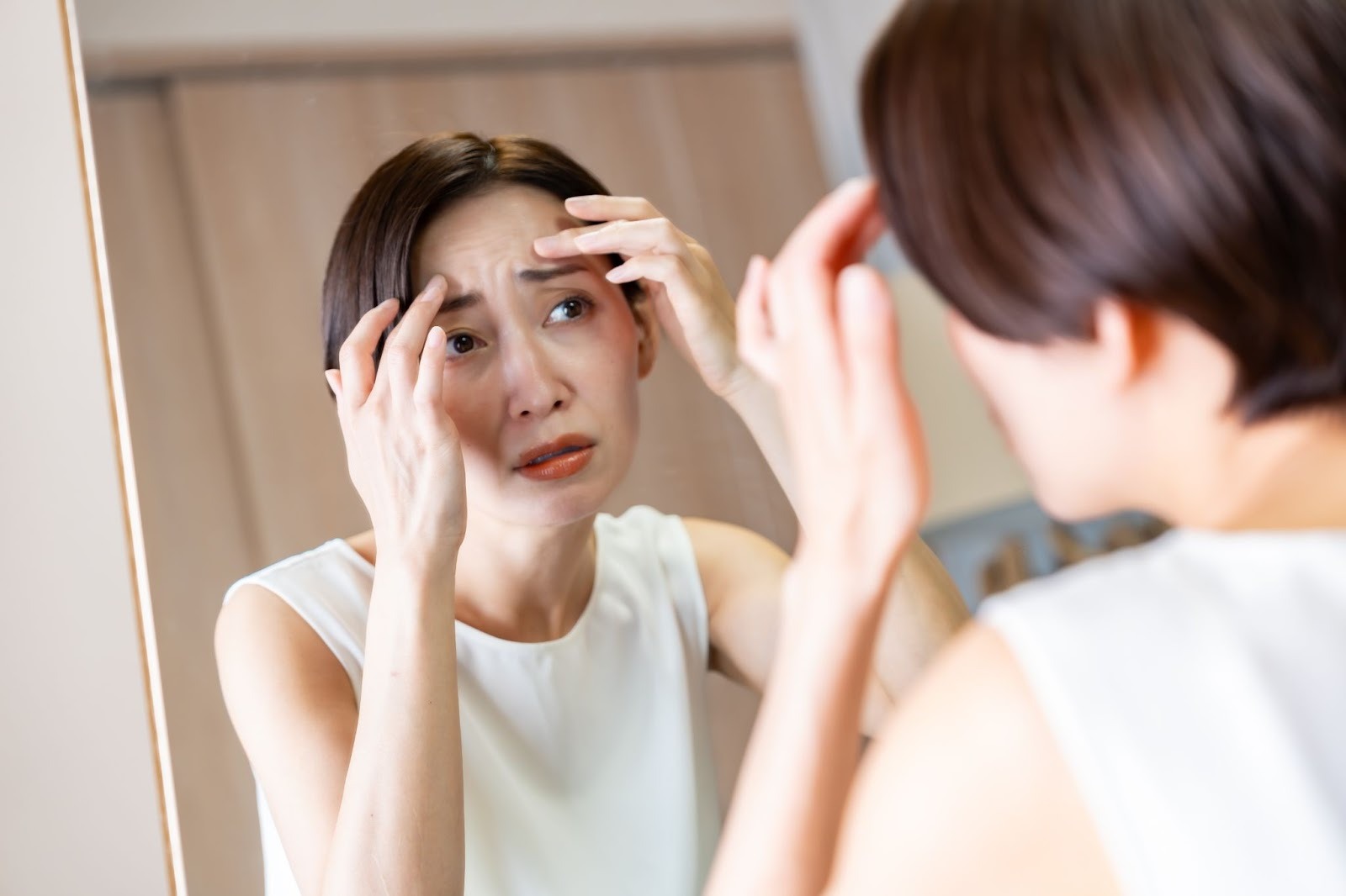 鏡を見ておでこのしわを気にしている女性