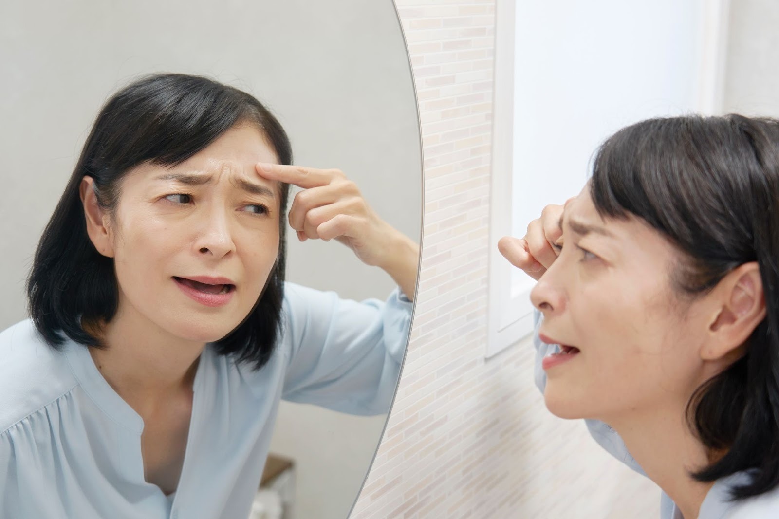 鏡を見ておでこのしわを気にしている女性