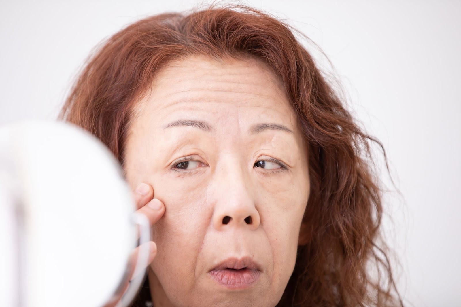 顔のたるみを気にして鏡を見ている女性