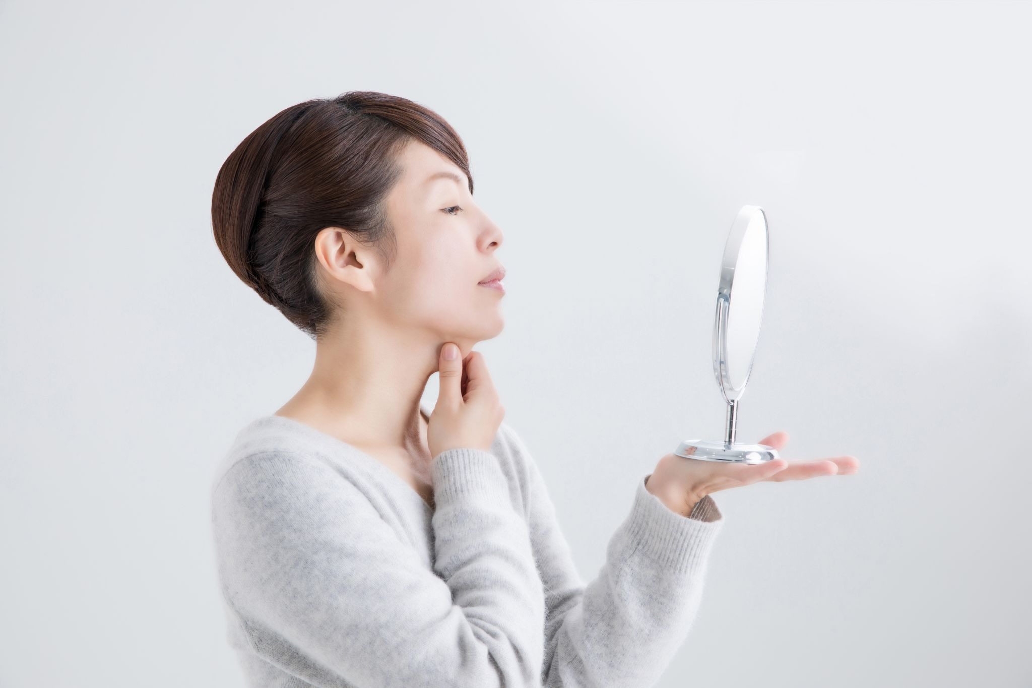 顎のたるみを気にして鏡を見ている女性