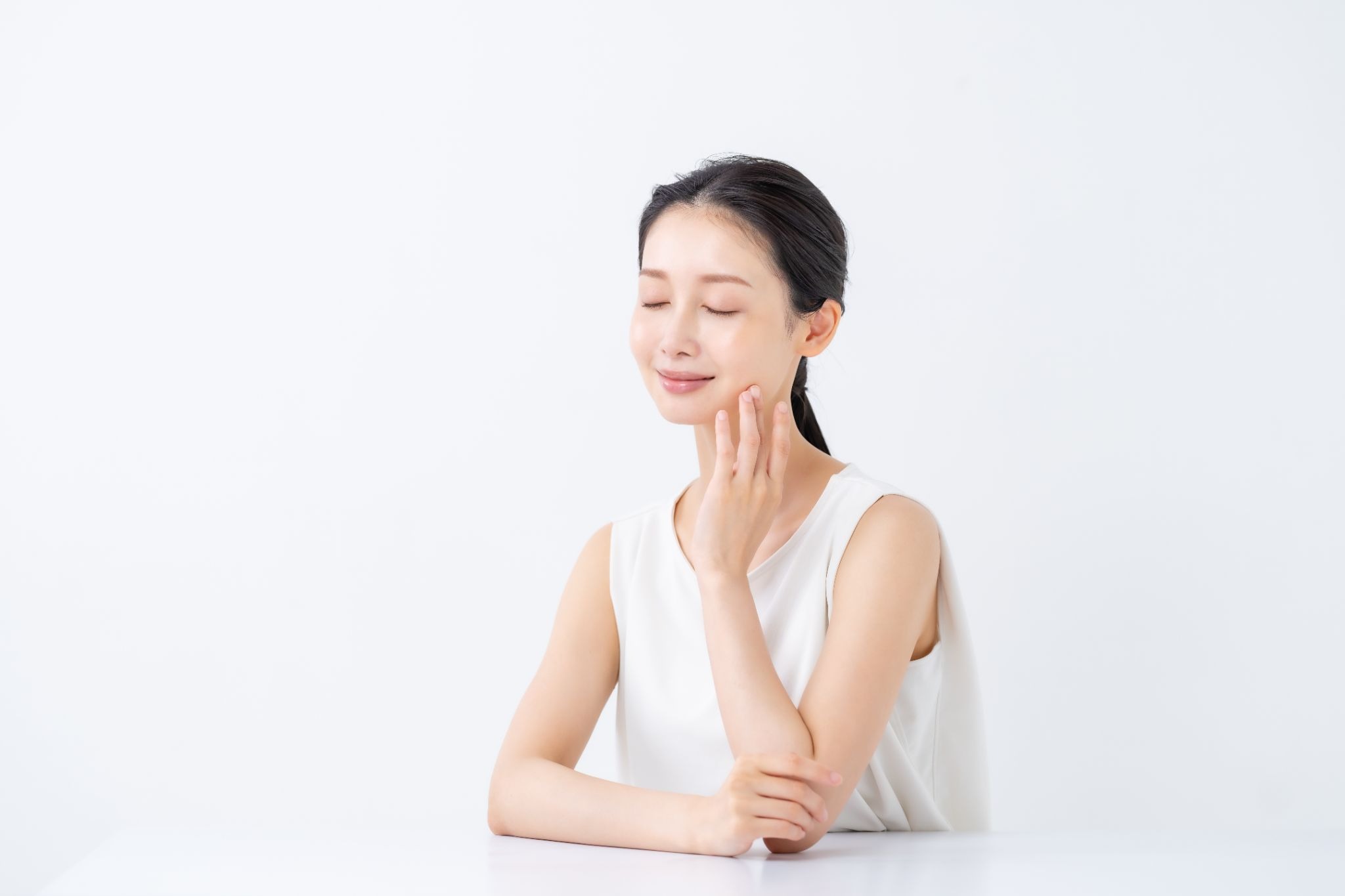 目を閉じて頬に触れている美肌の女性