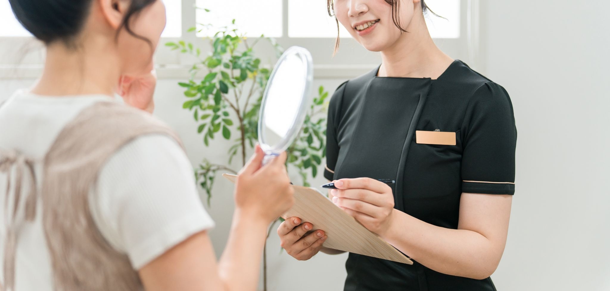 鏡を見ている女性と美容クリニックのスタッフ