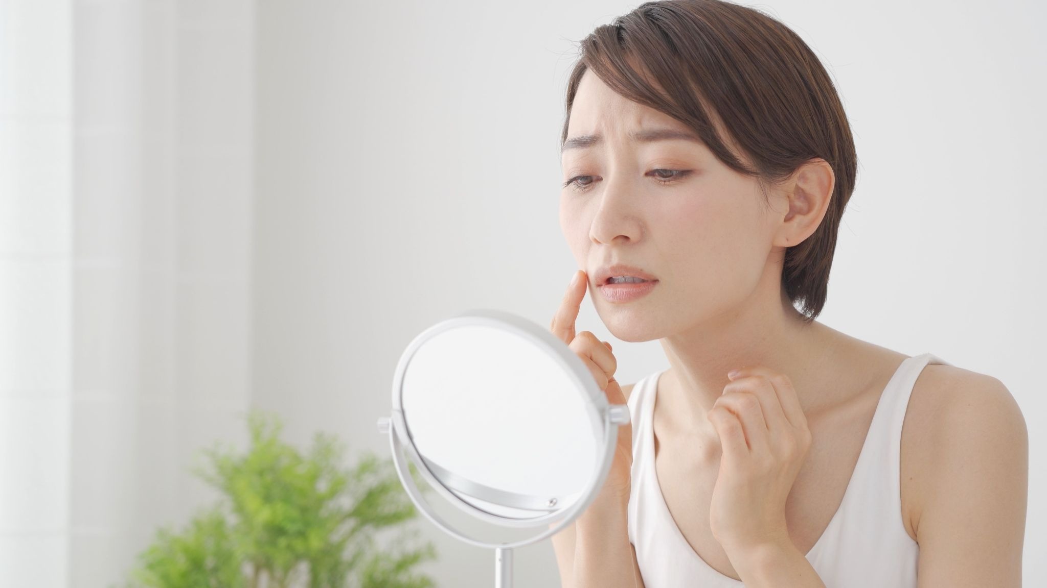 顔のたるみを気にして鏡を見ている女性